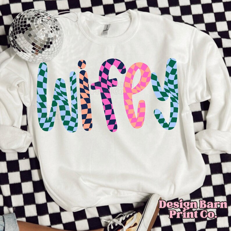 May include: White sweatshirt with the word "wifey" written in colorful, checkered letters. The letters are in a playful, distorted font.