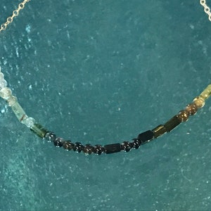 May include: A gold chain necklace with a graduated ombre of green, black, and white beads.