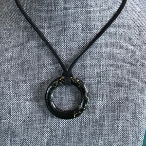 May include: A black leather cord necklace with a large black ring pendant. The ring has a gold swirl design.
