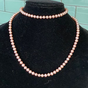 Może przedstawiać: Delikatny naszyjnik i choker z r&oacute;żowych pereł, prezentowane na czarnym manekinie. Małe, r&oacute;wnomiernie rozmieszczone perły tworzą klasyczny i elegancki wygląd. Tło z jasnoturkusowych płytek.