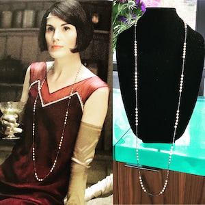 May include: A long pearl and black bead necklace on a black mannequin. The necklace is approximately 76 cm long.