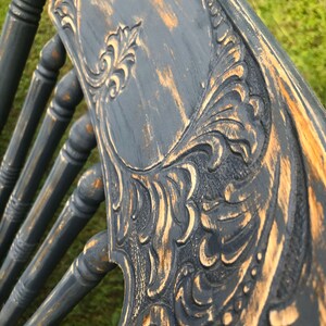 May include: Close-up of a dark blue wooden chair back with a carved floral design. The chair has been distressed with a light brown paint, giving it a vintage look.