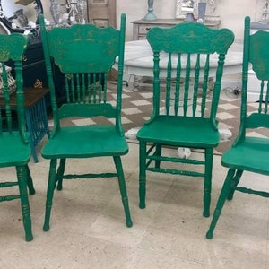 Pu&ograve; includere: Quattro sedie in legno verde con finitura usurata. Le sedie hanno uno schienale alto con un design intagliato e uno schienale a fuso.