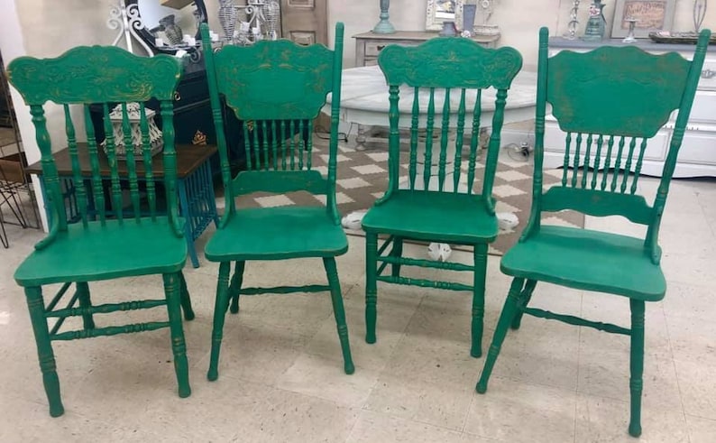Pu&ograve; includere: Quattro sedie in legno verde con finitura usurata. Le sedie hanno uno schienale alto con un design intagliato e uno schienale a fuso.