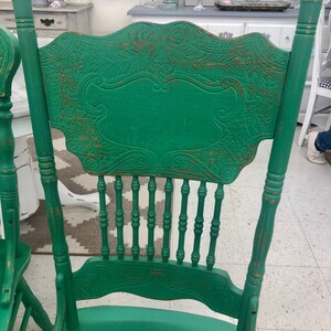 Pu&ograve; includere: Una sedia in legno verde con schienale intagliato e finitura usurata. La sedia ha uno schienale a fuso e una parte superiore curva.