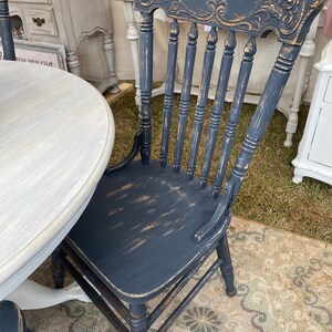 May include: A black wooden chair with a distressed finish and carved details on the back. The chair has a spindle back and a simple, rectangular seat.