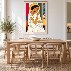 May include: A framed wall art print featuring a stylized illustration of a person in a white robe holding a swaddled infant. The artwork uses bold blocks of red, blue, and yellow, with a golden halo behind the person's head and a palm tree.