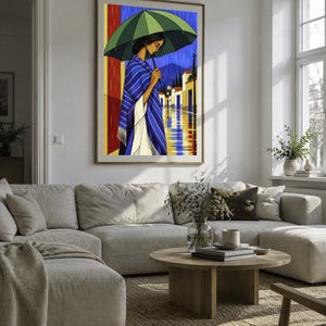 May include: A framed wall art print depicting a person standing under a large green umbrella during a rainstorm. The person wears a blue and white striped shawl over a white garment. The background shows a street with buildings and mountains.
