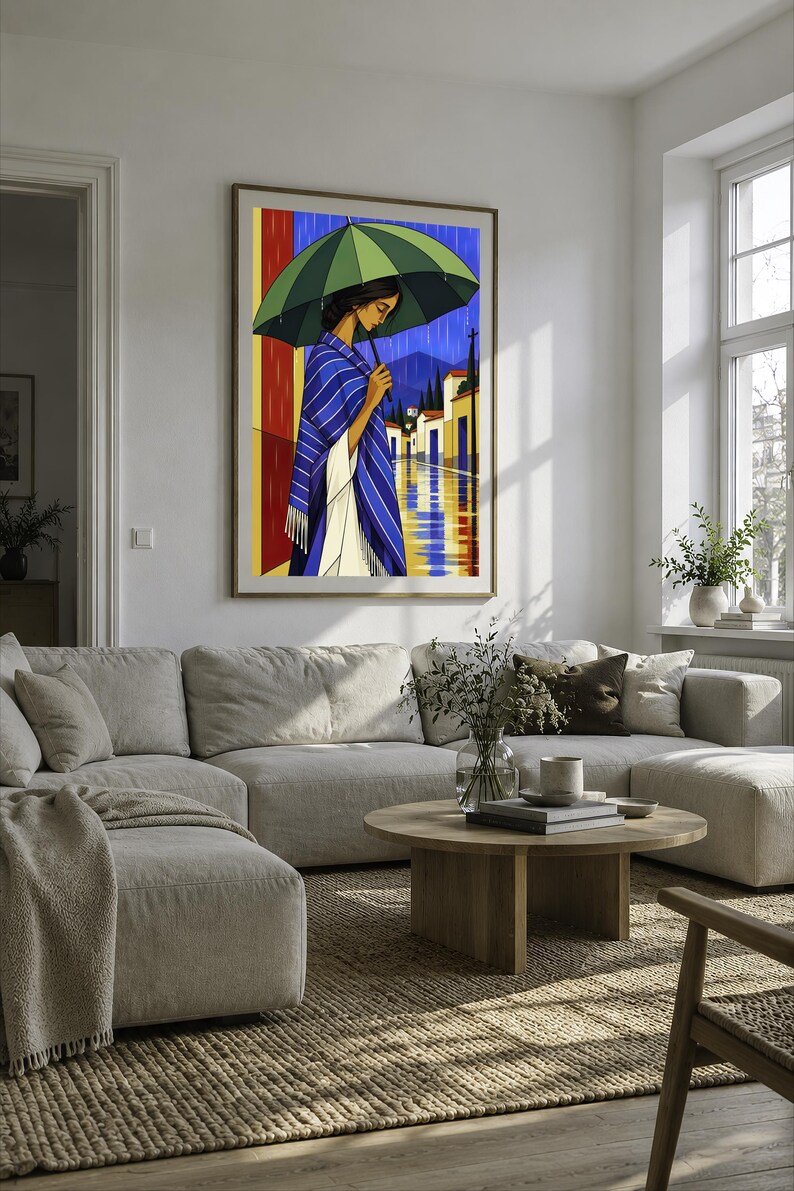 May include: A framed wall art print depicting a person standing under a large green umbrella during a rainstorm. The person wears a blue and white striped shawl over a white garment. The background shows a street with buildings and mountains.