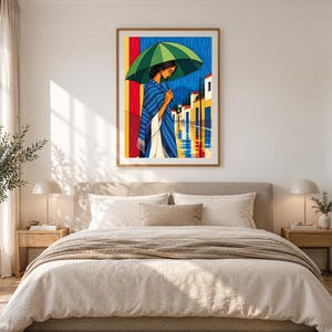 May include: A framed wall art print depicting a person standing in the rain under a large green umbrella. The person wears a blue and white striped shawl over a white garment. The background shows a street with colorful buildings.