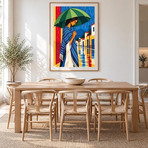 May include: A framed vertical art print depicting a person standing under a large green umbrella during a rainstorm. The person wears a blue and white striped shawl over a white garment. The background shows a street with buildings and reflections.