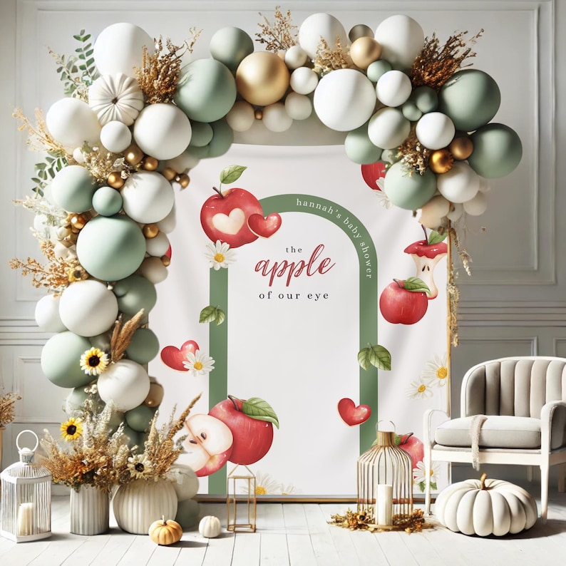 Puede incluir: Decoraci&oacute;n de baby shower con un arco de globos en blanco, verde salvia y dorado. El tel&oacute;n de fondo incluye un letrero con el texto "hannah's baby shower" y "the apple of our eye" con ilustraciones de manzanas y corazones. Las calabazas y flores decorativas completan la escena.