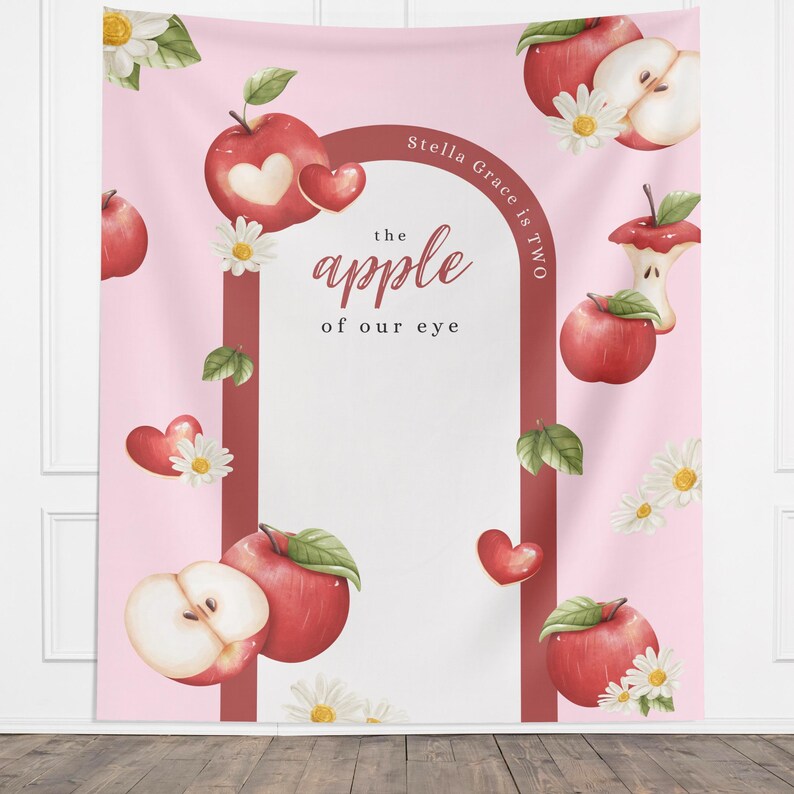 Puede incluir: Un tel&oacute;n de fondo rosa con un dise&ntilde;o de acuarela con manzanas rojas, margaritas y corazones. El texto "the apple of our eye" se muestra en una fuente decorativa. Tambi&eacute;n son visibles las palabras "Stella Grace is Two".