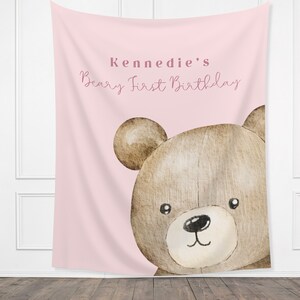 Może przedstawiać: R&oacute;żowe tło z tkaniny z akwarelową ilustracją twarzy misia. Tekst "Beary First Birthday Kennedie" jest napisany kursywą. Miś jest brązowy z białym pyskiem.