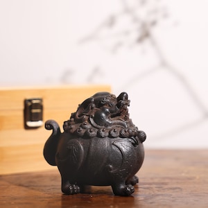 May include: A black ceramic incense burner shaped like a mythical creature with intricate details. The burner has a round body with a dragon-like head on top and four legs.