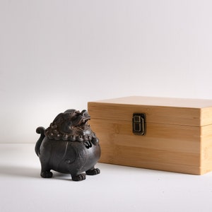 May include: A black ceramic incense burner shaped like a mythical creature with intricate details. The burner is sitting on a white surface next to a wooden box with a brass latch.