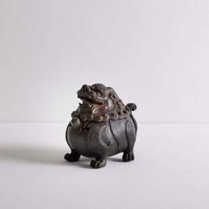 May include: A dark brown, intricately carved incense burner shaped like a mythical lion with a detailed face and curled tail.