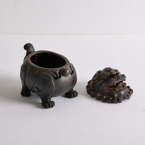 May include: A black ceramic incense burner with a lid shaped like a lion's head. The burner has intricate details and is decorated with floral patterns.