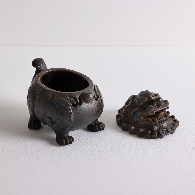 May include: A black ceramic incense burner with a lid shaped like a lion's head. The burner has intricate details and is decorated with floral patterns.