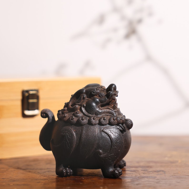 May include: A black ceramic incense burner shaped like a mythical creature with intricate details. The burner has a round body with a dragon-like head on top and four legs.