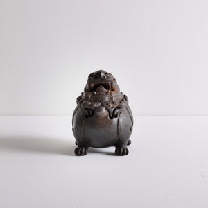 May include: A dark brown ceramic incense burner shaped like a lion with intricate details and a carved open mouth.