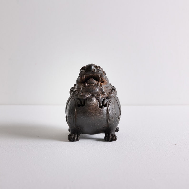 May include: A dark brown ceramic incense burner shaped like a lion with intricate details and a carved open mouth.