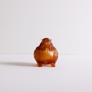 May include: A small, amber-colored, intricately carved, ceramic incense burner in the shape of a mythical creature with a round body and a lid.