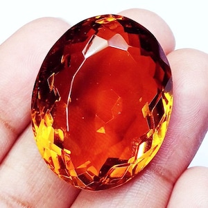 May include: A large, oval-shaped, faceted gemstone with a deep orange color. The gemstone is cut with many facets, giving it a brilliant shine.