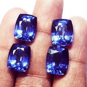 May include: Four cushion-cut gemstones with a deep, vibrant blue color and faceted surfaces that reflect light. These loose stones are arranged in a square formation, showcasing their transparent quality and polished, symmetrical edges.