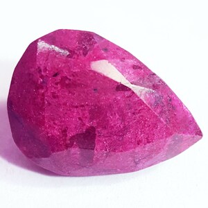 Könnte beinhalten: Ein tiefrosa birnenförmiger Edelstein mit facettiertem Schliff. Der Edelstein hat eine raue, strukturierte Oberfläche.