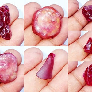 May include: A collection of six distinct raw ruby gemstones in various shapes and sizes. The stones exhibit deep red and translucent pink hues with natural crystalline textures, jagged edges, and smooth, polished surfaces across the set.