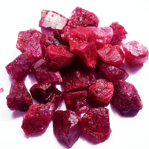 May include: A pile of loose, raw ruby gemstones. The rubies are a deep red colour and have a variety of shapes and sizes.