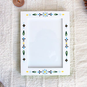May include: White picture frame with a blue, yellow, green and black floral design around the border.