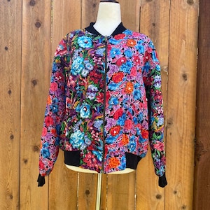 May include: A black bomber jacket with a floral print in shades of pink, blue, and red. The jacket has a zipper closure and a ribbed collar, cuffs, and hem.