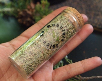 May include: A glass jar with a cork lid filled with dried herbs. The jar has a black label that reads "Mountain Spice Co."