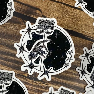 May include: Black and white sticker with a skeletal hand reaching out of a starry sky, surrounded by barbed wire and a rose.