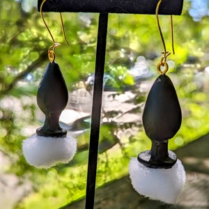 Può includere: Un paio di orecchini neri e bianchi con un pon pon bianco soffice nella parte inferiore di ogni orecchino.