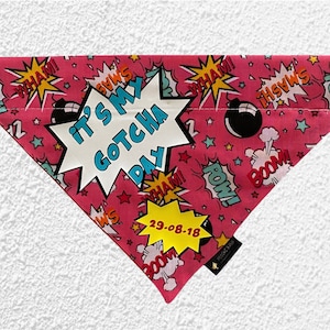 May include: A pink dog bandana with a comic book design. It displays speech bubbles with words such as "WHAM!" and "POW!", alongside the text "IT'S MY GOTCHA DAY" and the date "29-08-18".