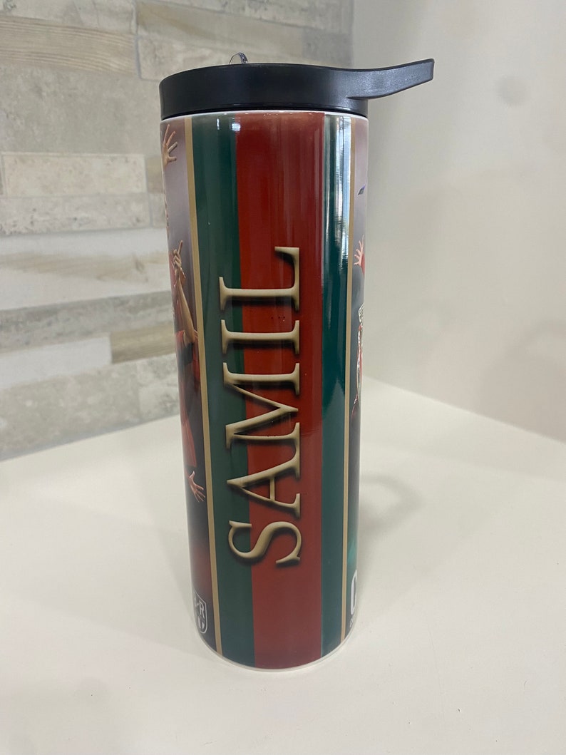 May include: A red, green, and gold striped stainless steel tumbler with a black lid and a black straw. The tumbler has the word "SAMII" printed on it.