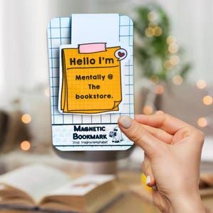 Peut inclure: Signet magnétique jaune avec un post-it qui dit "Hello I'm Mentally @ The bookstore." Le signet a un petit cœur et un fantôme. Le texte "Magnetic Bookmark" et "Shop: ImagineAlphabet" sont également sur le signet.