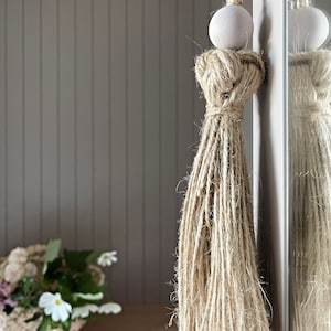 Peut inclure: Un cordon en fibre naturelle avec une perle blanche suspendue à une porte ou un mur. Le cordon est fait de fibres naturelles et présente un motif noué.