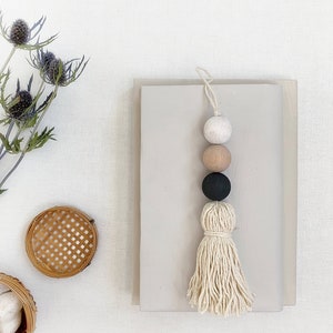 May include: A beige, black, and brown wooden bead garland with a white tassel hanging from a book. The garland is made of three beads and a tassel.
