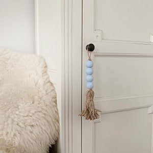 May include: A light blue beaded garland with a brown tassel hanging from a white door with a black door knob.