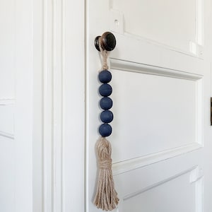 Op de afbeelding: Een donkerblauwe kralen deurkwast met een natuurlijke jute kwast die aan een deurklink hangt.
