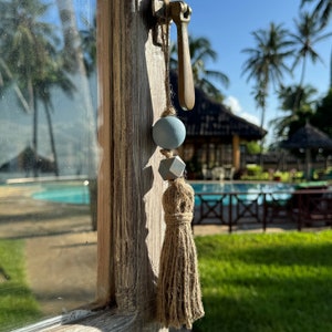 Könnte beinhalten: Ein blauer und grauer Quaste, der an einem Türgriff hängt. Die Quaste ist aus Stoff und hat oben eine Holzperle. Der Türgriff ist aus Metall und hat eine Messing-Oberfläche.