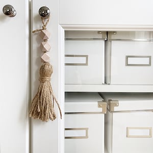 May include: White cabinet with six white storage boxes with silver hardware. A wooden tassel with pink beads hangs from the top of the cabinet door.