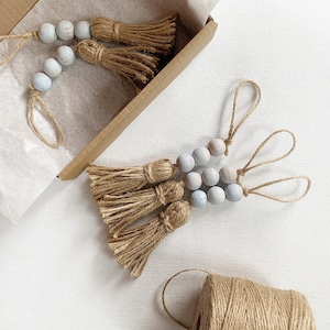 May include: A set of three light blue wooden bead garlands with natural jute tassels. Each garland has a different length and is tied with a natural jute string.