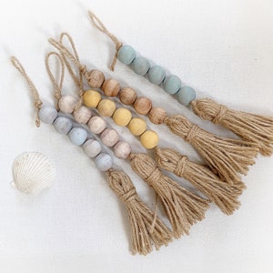 Könnte beinhalten: Fünf Stränge aus Holzperlen mit Quasten. Die Perlen sind in Blautönen, Gelb und Braun. Die Quasten sind aus Naturfaser.