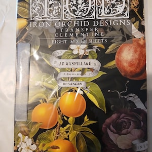 Può includere: Una confezione di fogli transfer Iron Orchid Designs Clementine. La confezione presenta uno sfondo scuro con illustrazioni di arance, melograni e rose. Il testo include "Iron Orchid Designs", "Transfer Clementine" e "Otto fogli da 20,3 cm x 30,5 cm".
