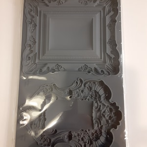 May include: A grey silicone mould for decorative frames. The mould features two ornate frame designs with floral and scroll details. The packaging reads "IRON ORCHID DESIGNS MOULD 'FRAMES II'" and includes the brand's logo at the top.